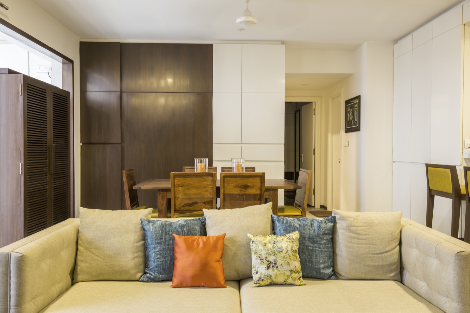 Living room with a sectional sofa and floor-to-ceiling wood-and-lacquer wardrobe paneling by WOODWORKS Interior, Bengaluru