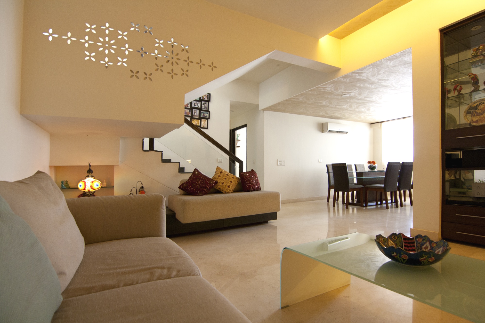 Open-plan living and dining space with a floating staircase, warm cove lighting and marble flooring by WOODWORKS Interior, Bengaluru