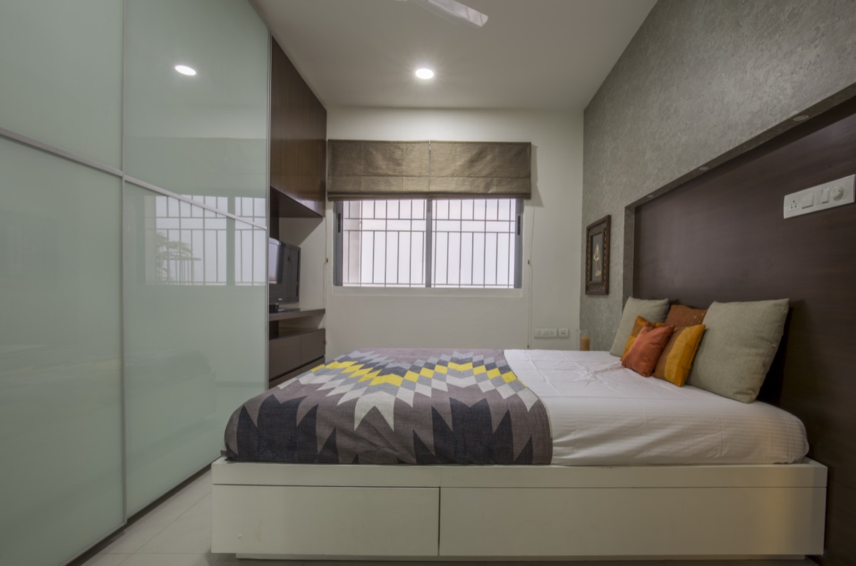 Master bedroom with a textured accent wall, upholstered platform bed and frosted-glass sliding wardrobe by WOODWORKS Interior, Bengaluru